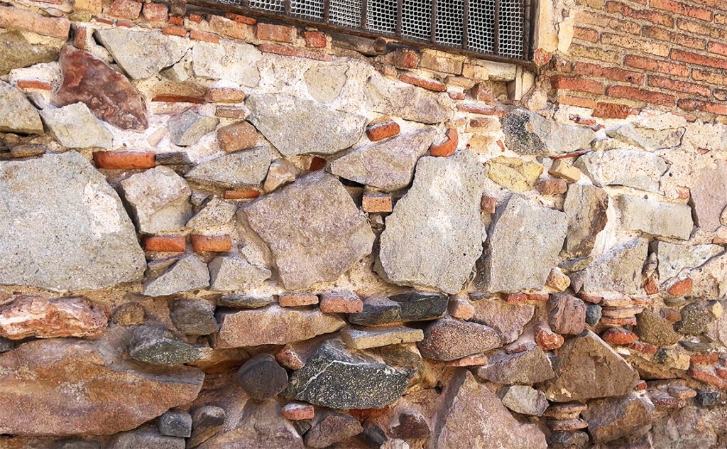 バルセロナ（Barcelona）ファブラ・イ・コーツ（Fabra i Coats）壁面下部のクローズアップで、石材の隙間にレンガの破片を詰め込んで補強した様子が観察できる